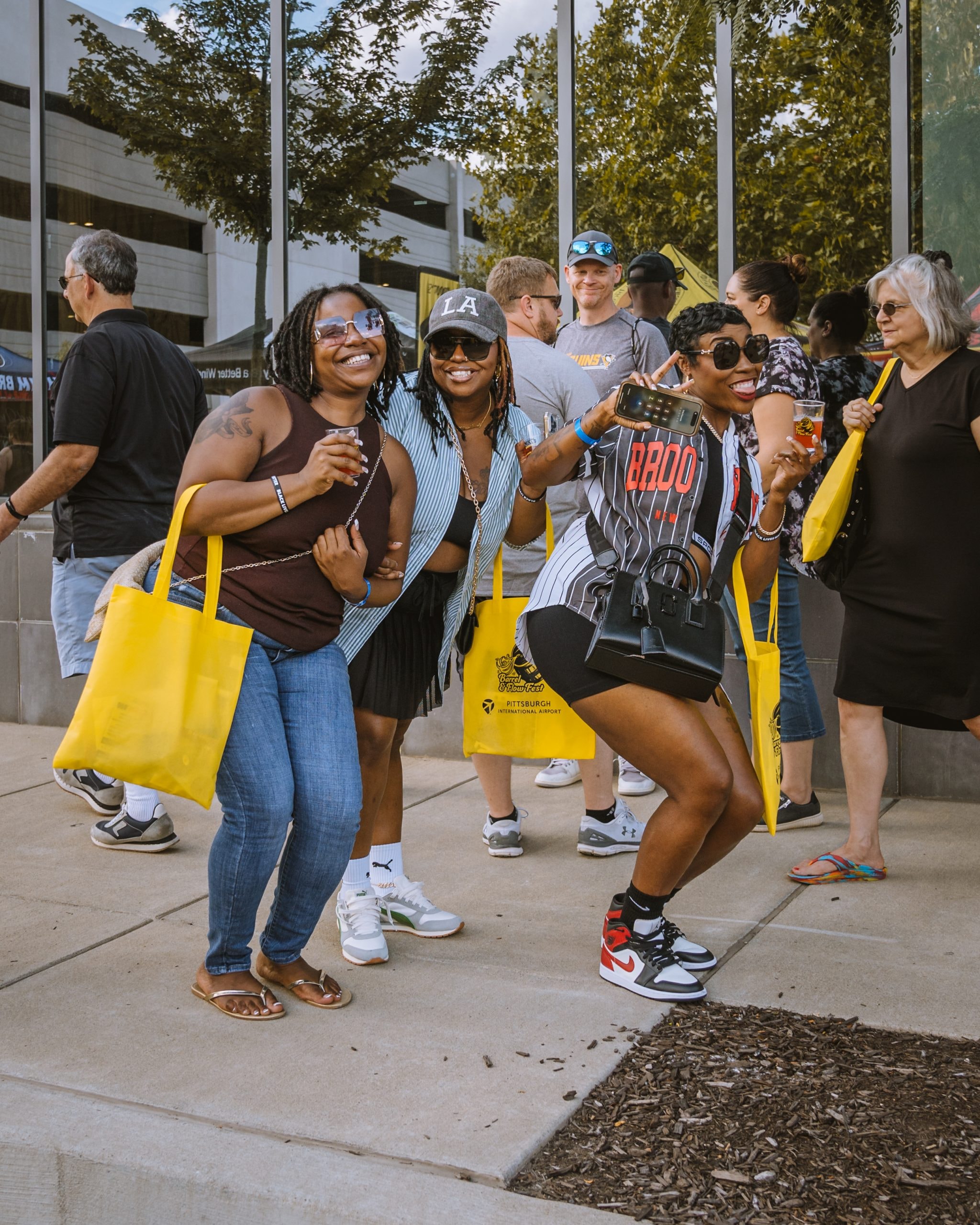 Three women celebrating at Barrel & Flow festival with yellow tote bags