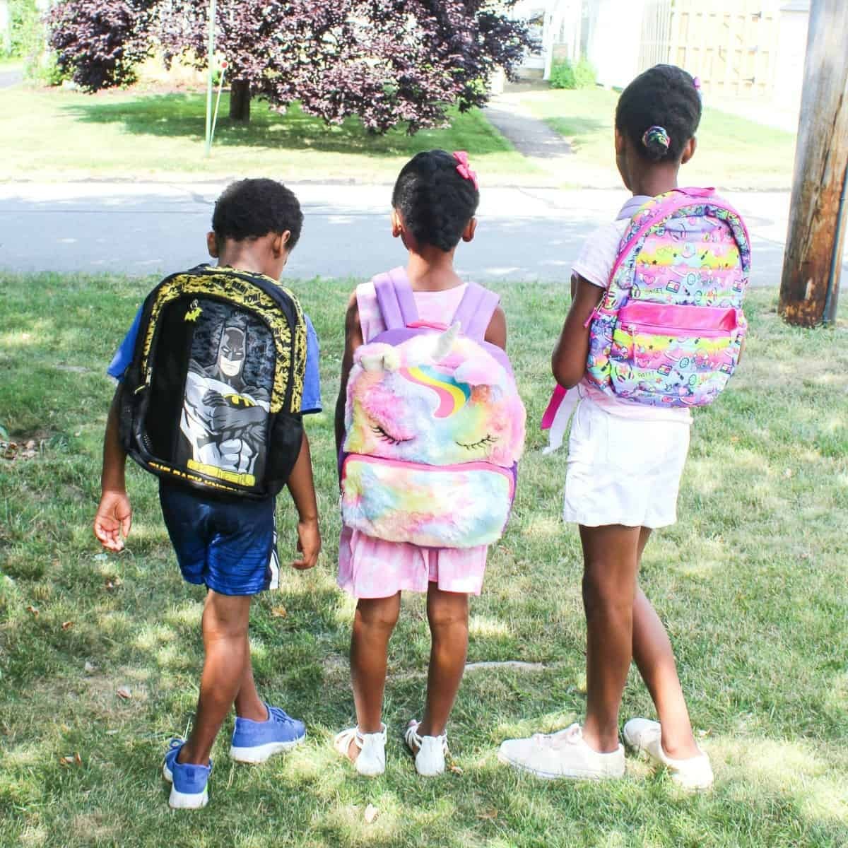 Three children wearing colorful backpacks ready for the new school year