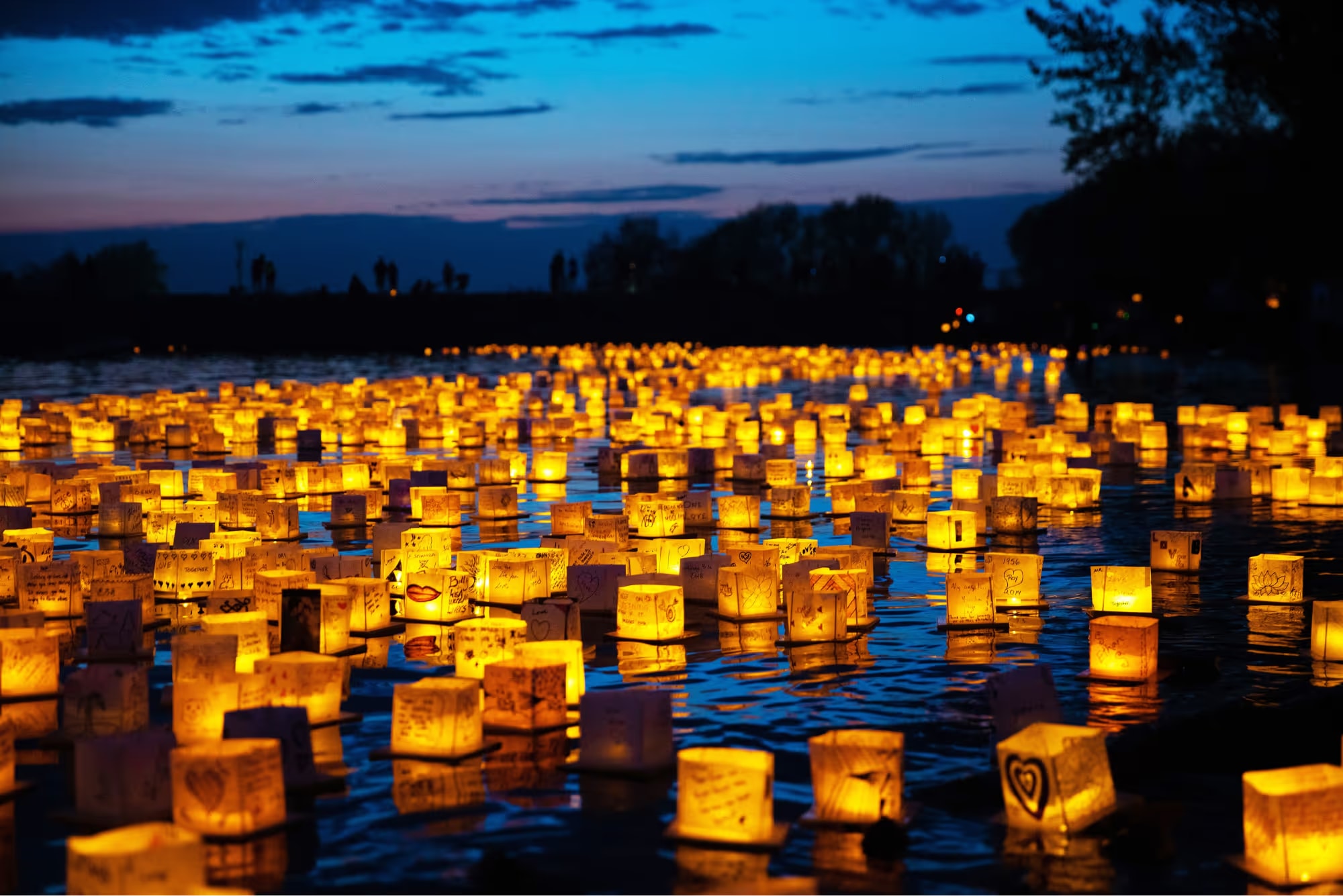 Thousands of glowing water lanterns floating on a dark river at dusk, Pittsburgh Water Lantern Festival