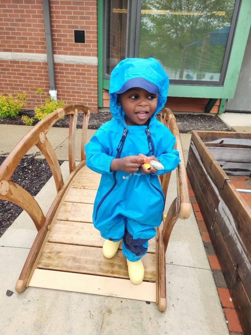 Young child in blue PNC Grow Up Great rainsuit on a wooden bridge