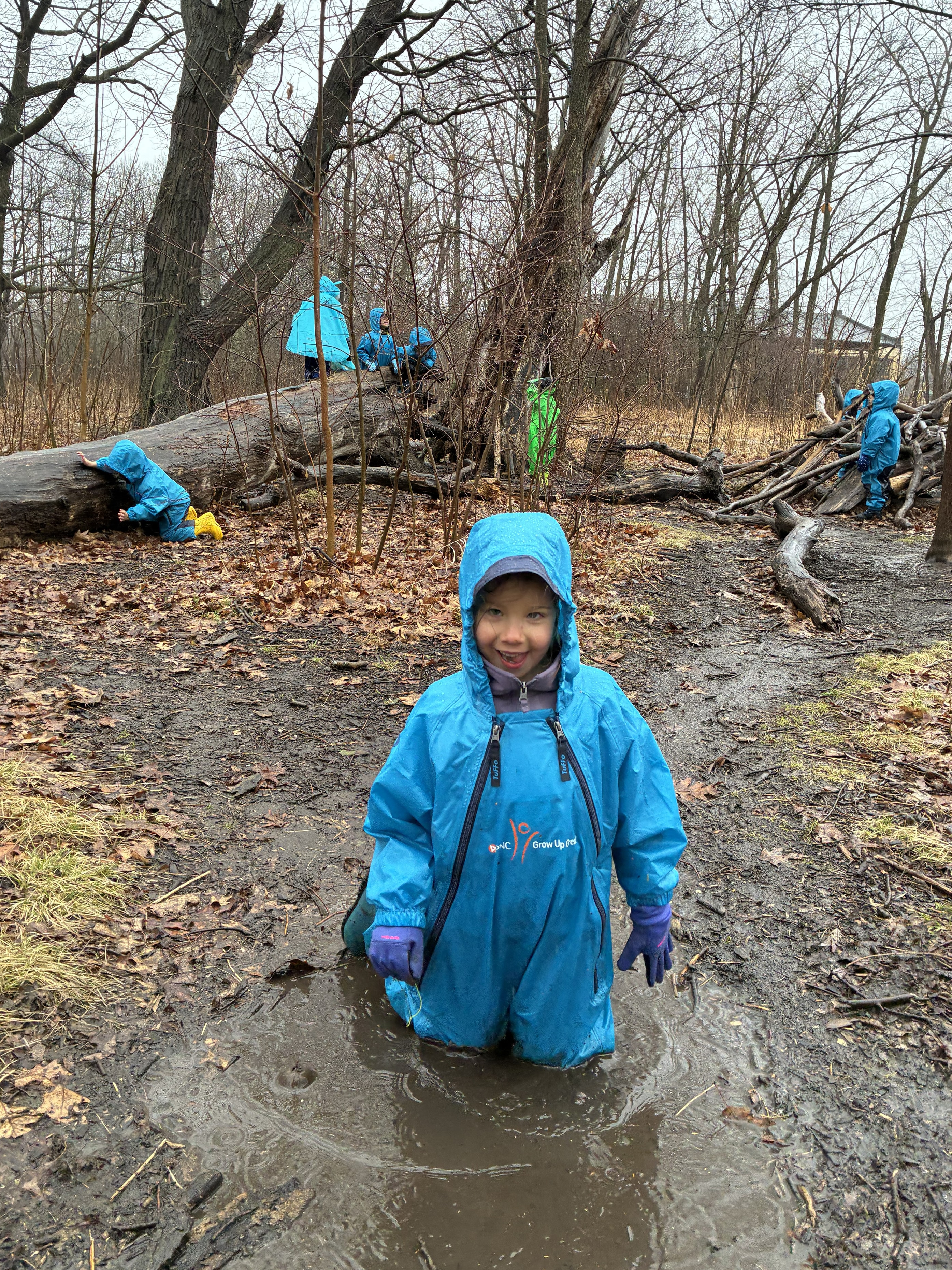 Child in Muddy Buddy waterproof suit exploring outdoors in a wooded area