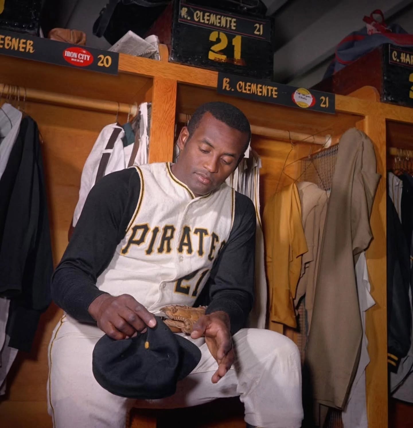 Roberto Clemente seated at his locker, No. 21 nameplate above him — color photo